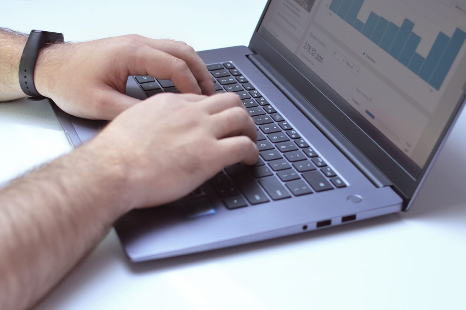 From above side view of crop unrecognizable male marketer working on netbook while using analytical software in office
